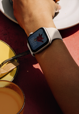 Arm einer Person, die nach etwas zum Frühstücken greift, Apple Watch SE 3 am Handgelenk, Aluminiumgehäuse in Polarstern, Always-On Display, Porträt einer Person auf dem Zifferblatt, Sportarmband in Polarstern